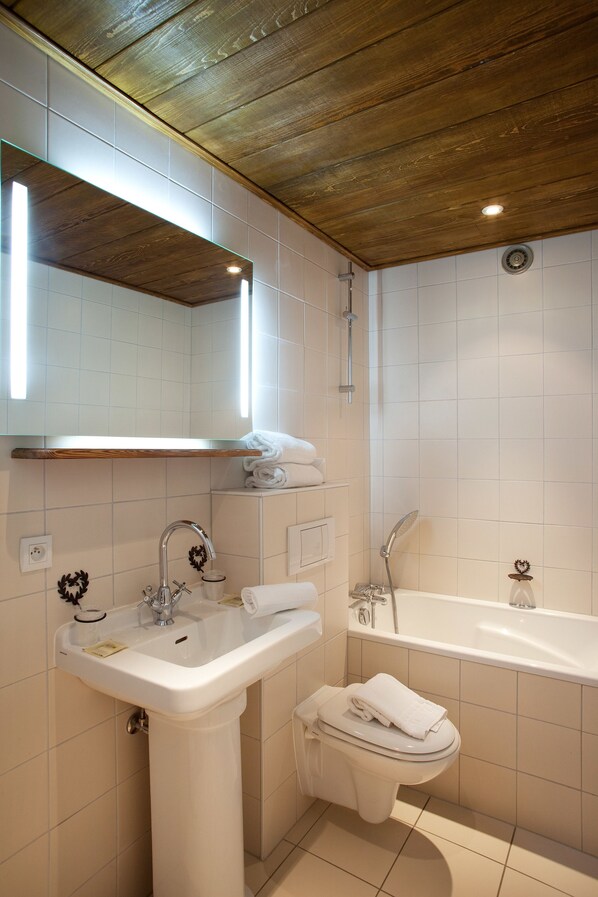 A bathroom with a wooden ceiling, white tiles, a sink, a toilet, and a bathtub. - Logis Hôtel Domaine de Rouffach (Rouffach)