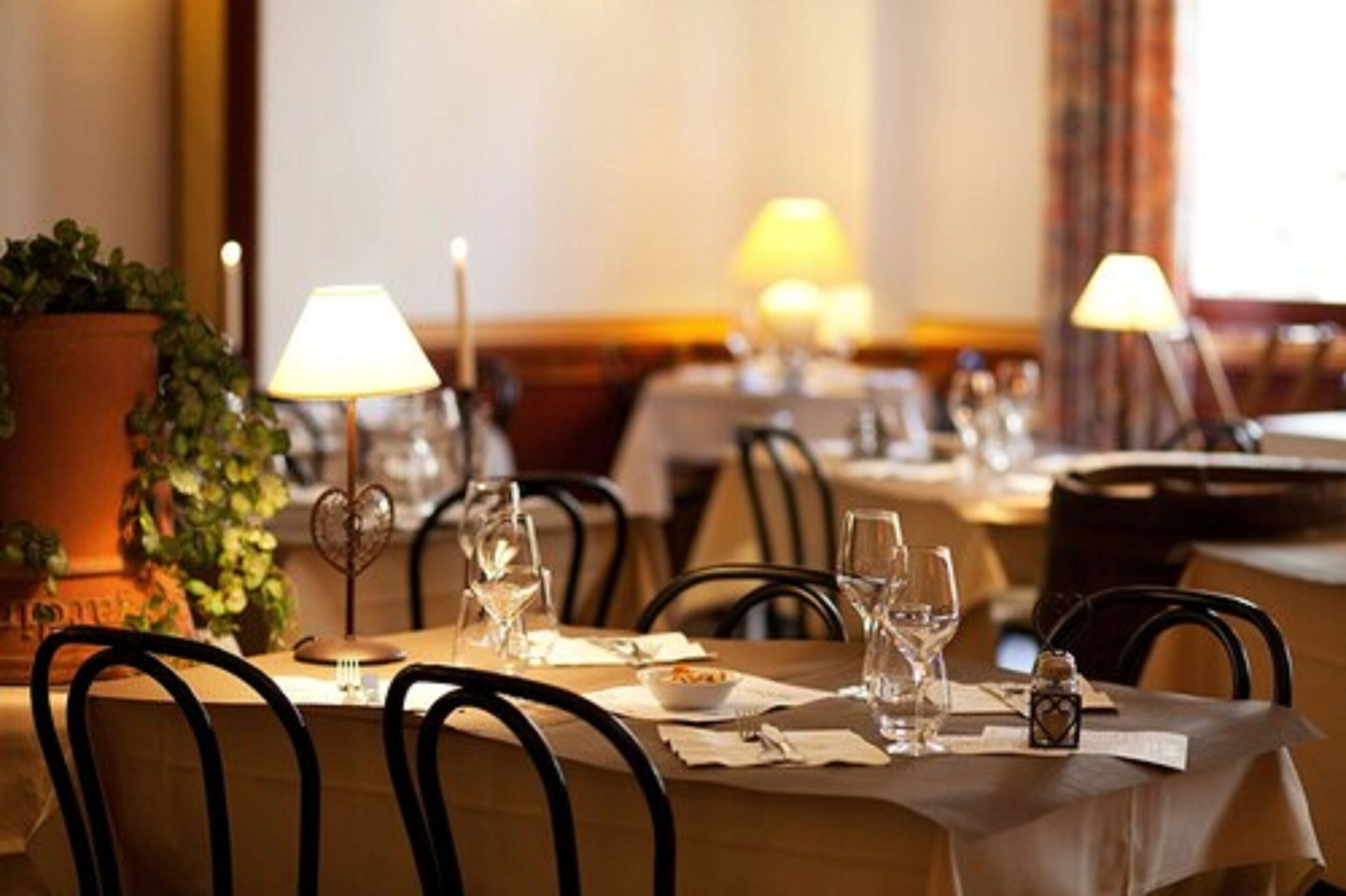 A dining area with tables set for two, each with a white tablecloth, wine glasses, and a small candle.