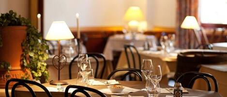 A dining area with tables set for two, each with a white tablecloth, wine glasses, and a small candle.