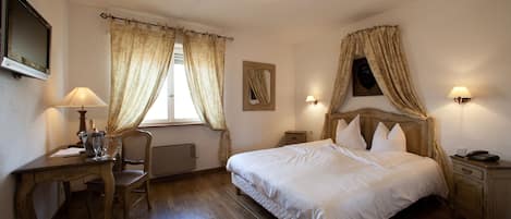 A bedroom with a wooden bed, a desk with a lamp, a chair, and a window with curtains.