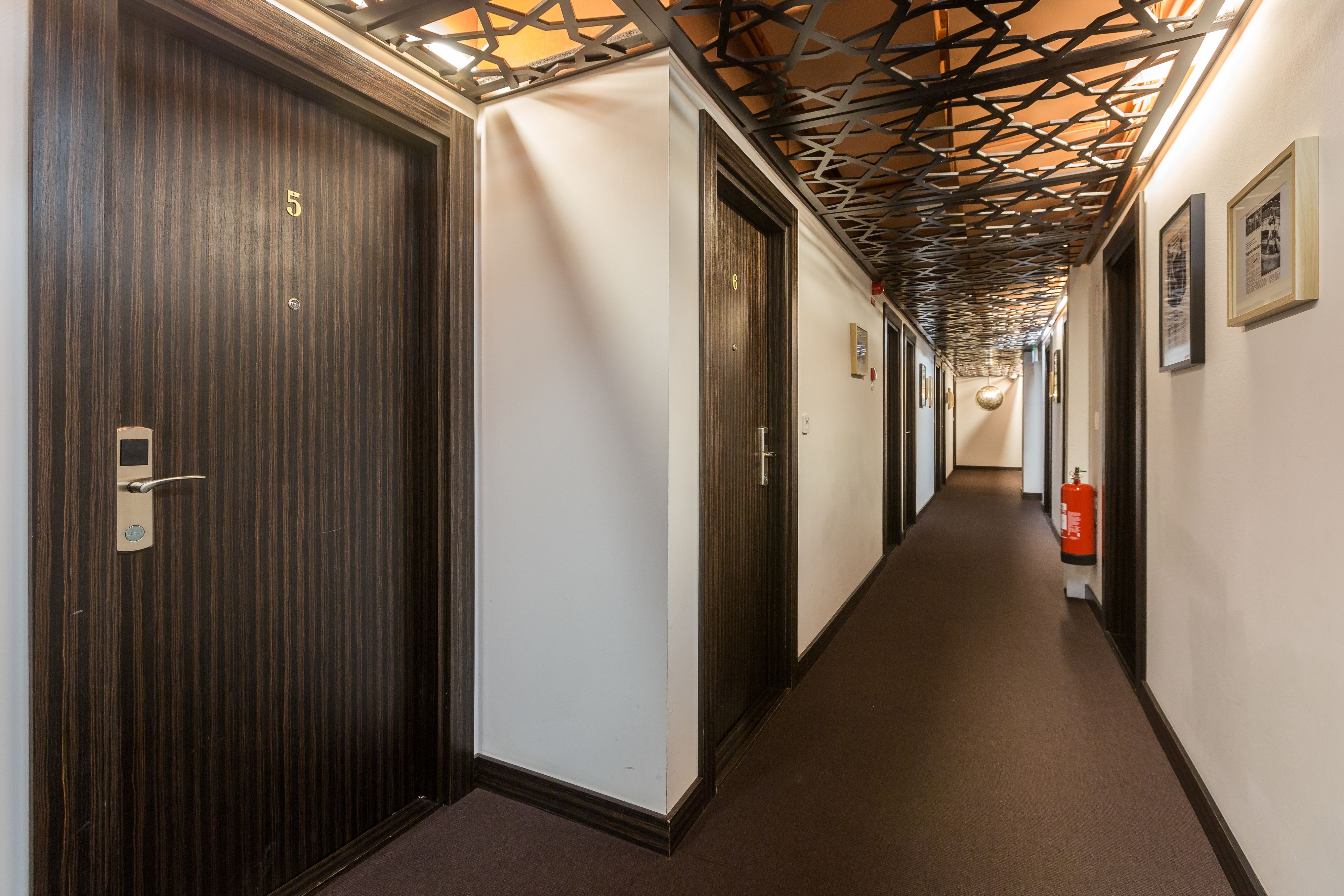 A hallway with wooden doors, a fire extinguisher, and framed pictures on the wall.