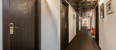 A hallway with wooden doors, a fire extinguisher, and framed pictures on the wall.