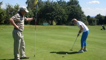 Ein Golfplatz mit Putting Green, Fahnenstock und Golfer, der zum Putt ansetzt.