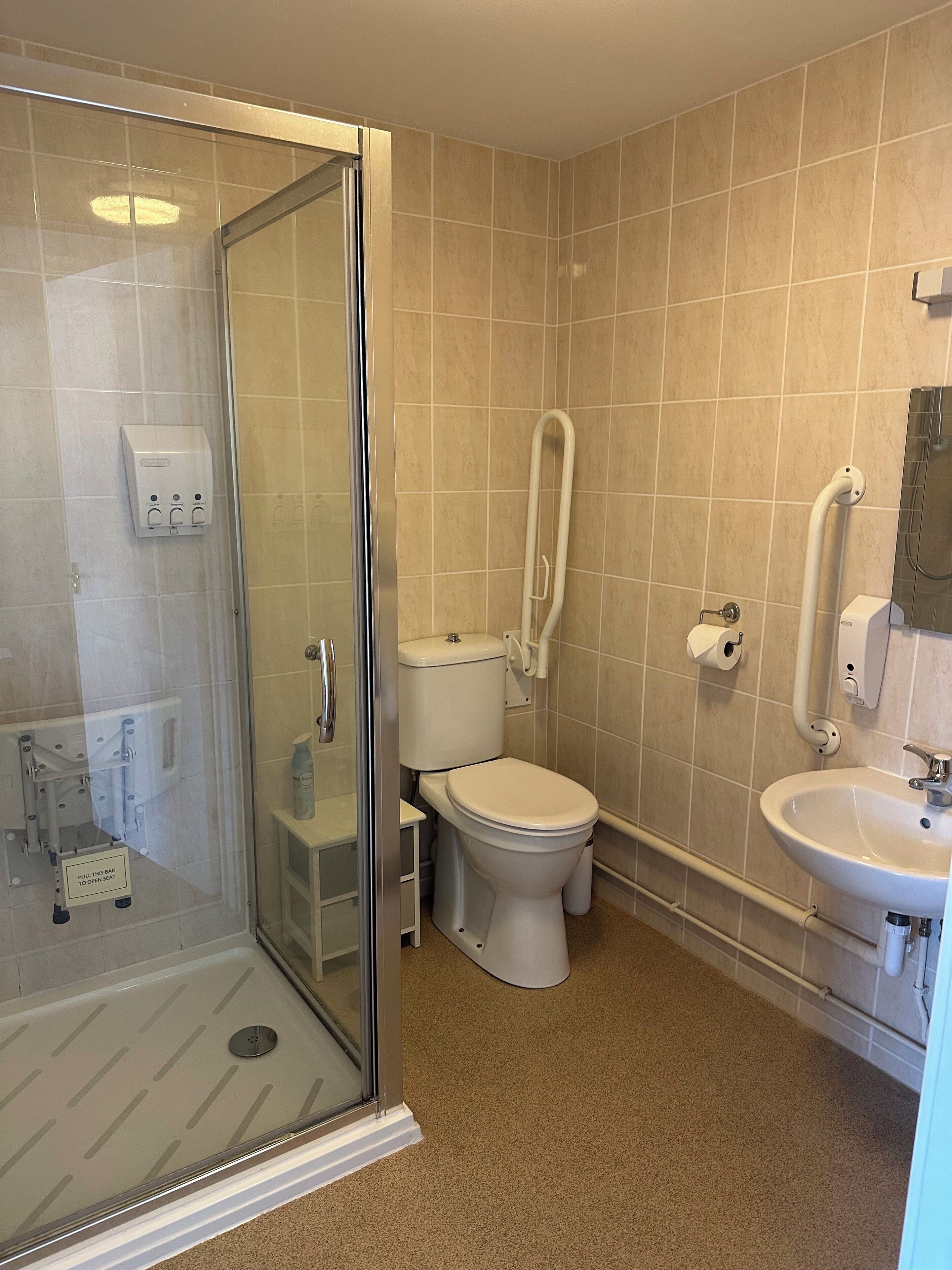 A bathroom with a glass-enclosed shower, a toilet, a sink, and a hand dryer.