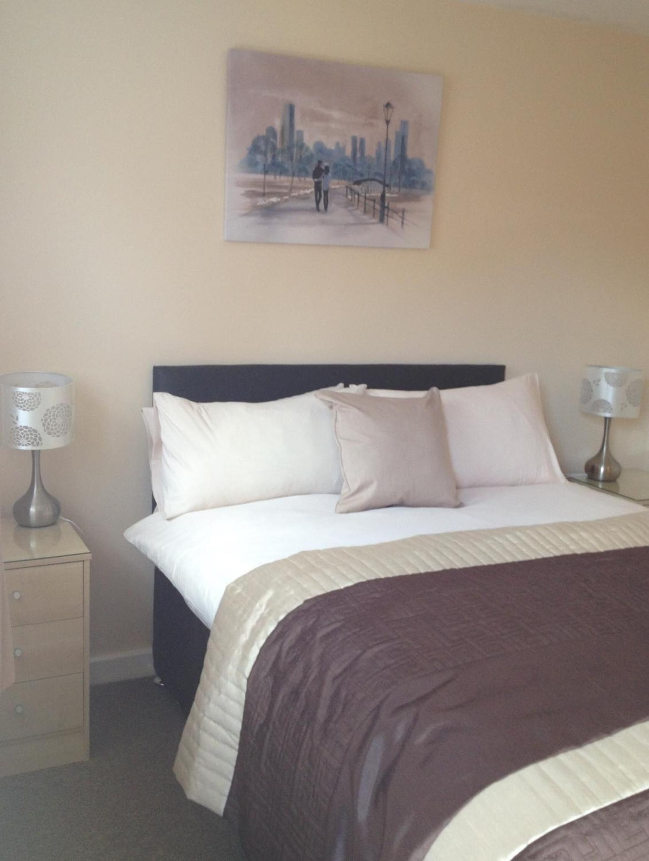 A hotel room with a bed, two bedside lamps, a nightstand, and a painting on the wall.
