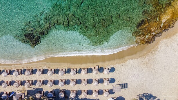 An aerial view of a beach with rows of sun loungers and a wooden walkway leading to the water. - Porto Koundouros Beach and Villas (Kea)