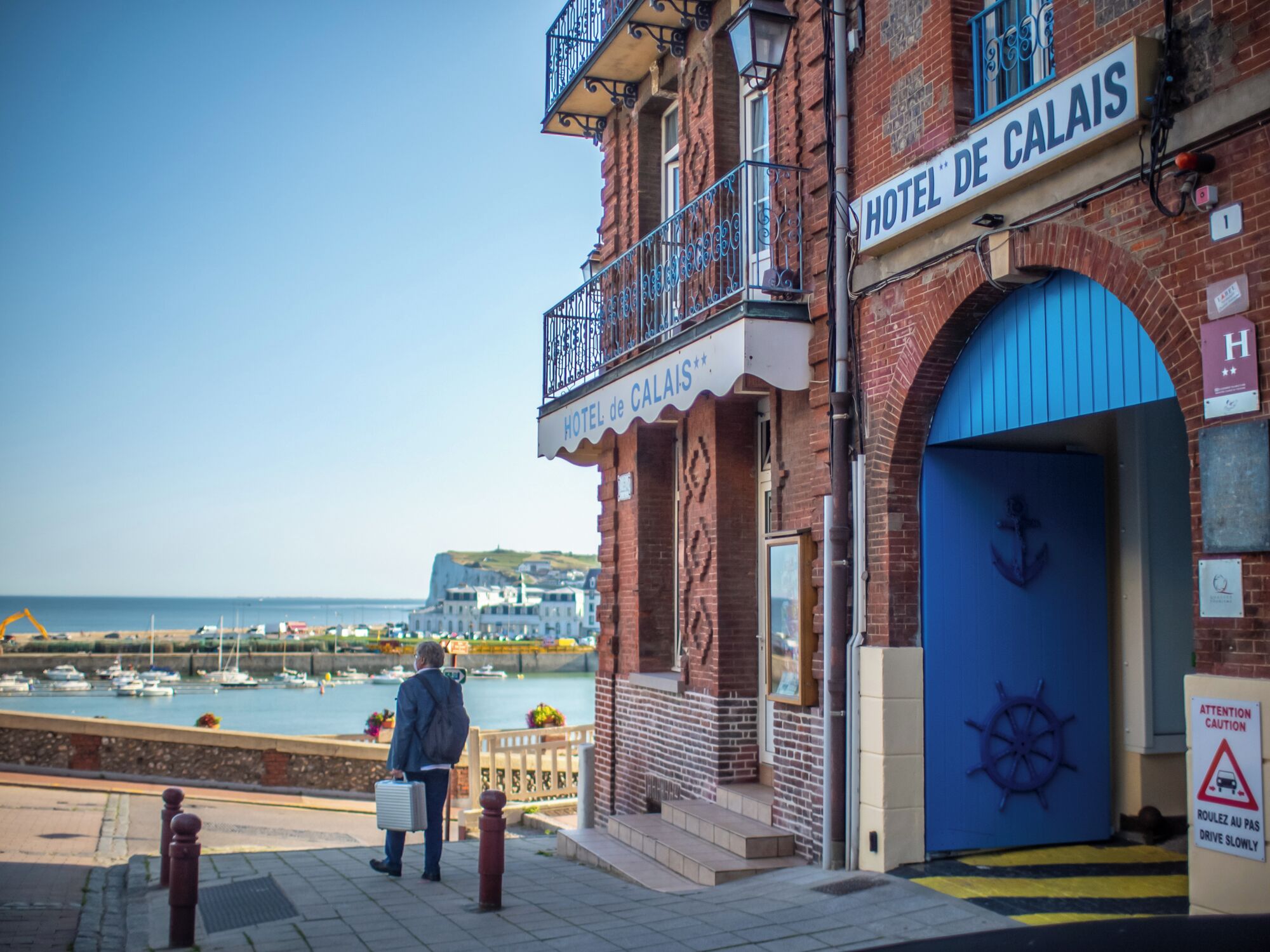 Un edificio histórico con un letrero que dice 'HOTEL DE CALAIS' y una puerta azul con un símbolo de ancla.