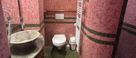 A bathroom with a tiled floor, a sink with a basin, a toilet, and a shower area.