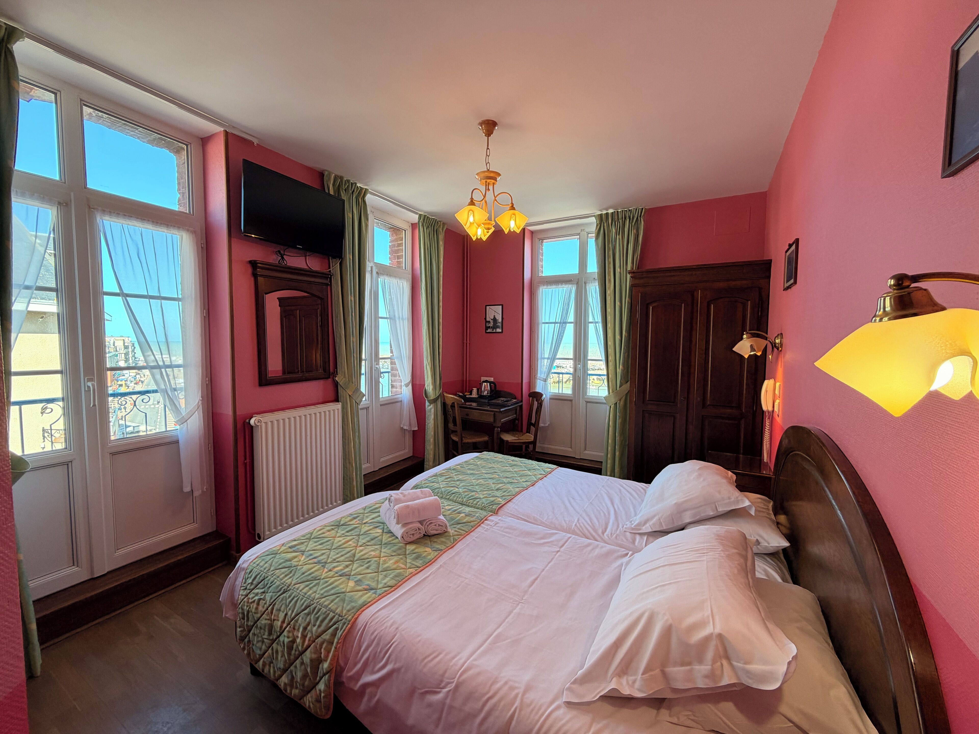 A hotel room with a bed, a desk, a chair, a wardrobe, a television, and a window with curtains.