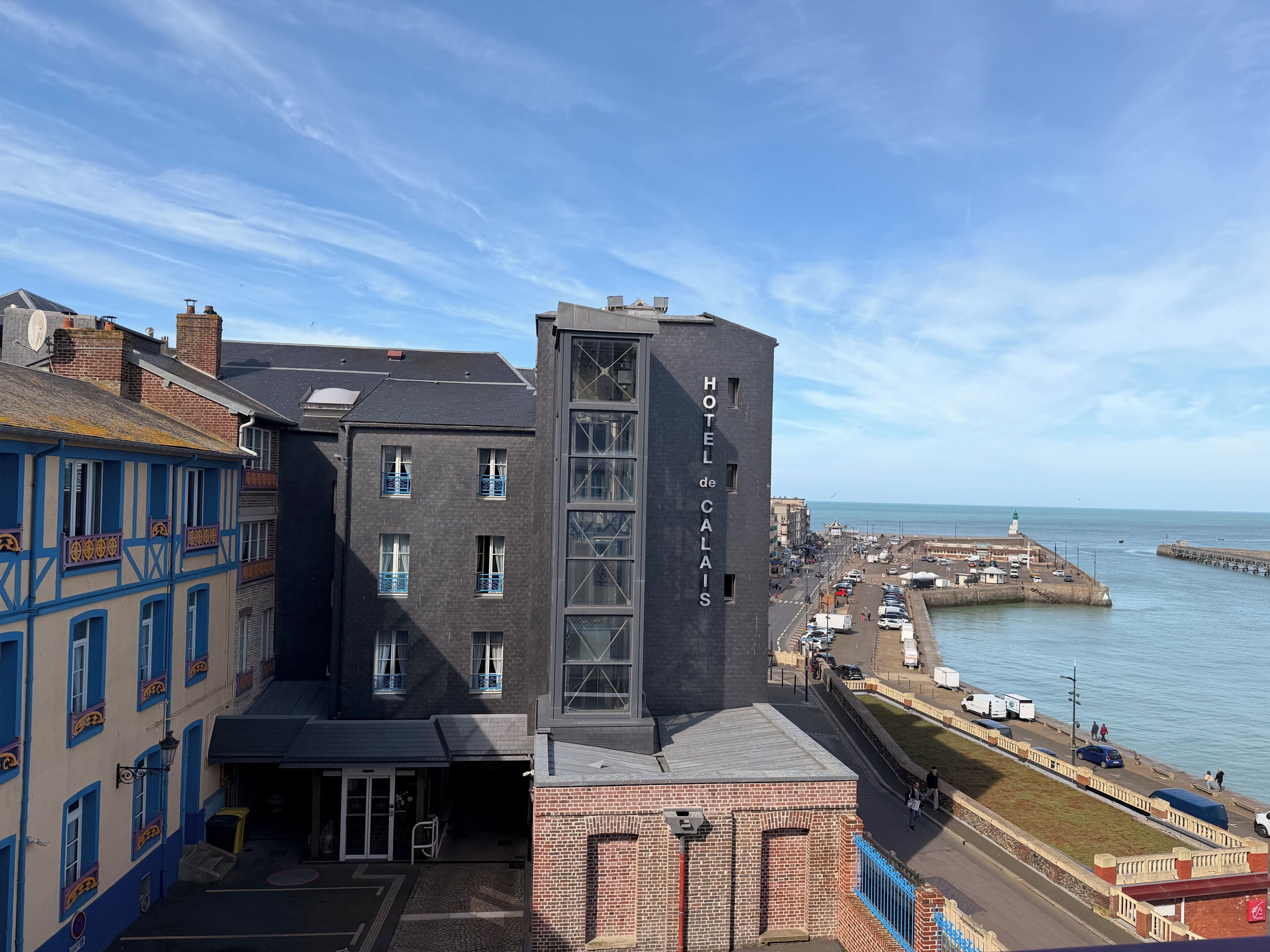 A hotel with a prominent tower, a waterfront view, and a street with parked cars.