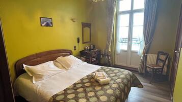 Une chambre d’hôtel avec un lit, un bureau, une chaise, une fenêtre avec des rideaux et un lustre.
