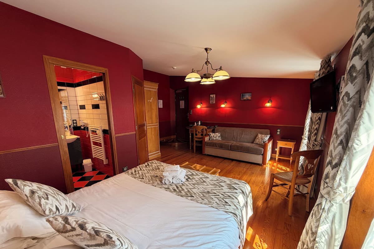 A hotel room with a bed, a sofa, a TV, and a wooden floor.