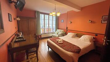 Habitación de hotel con una cama, un escritorio, una silla, un televisor montado en la pared y una ventana con cortinas.
