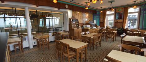 A restaurant with wooden tables and chairs, patterned floor tiles, and hanging pendant lights.