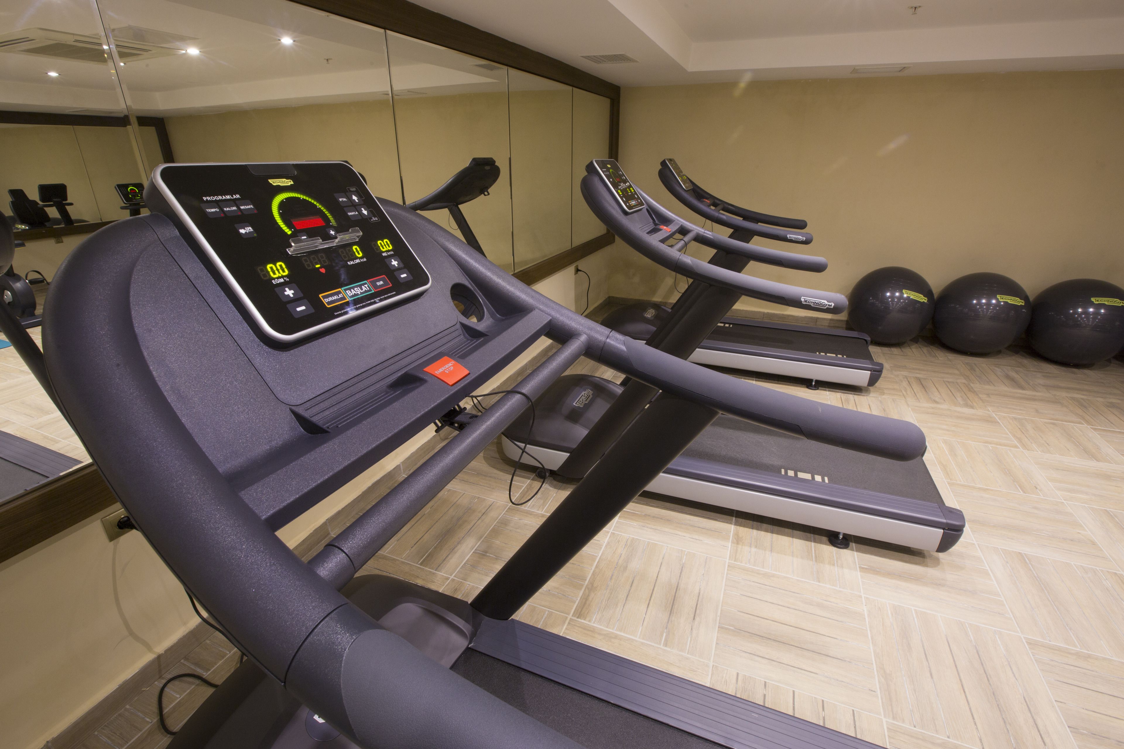 Een fitnessruimte met loopbanden, trainingsballen en een digitaal scherm.