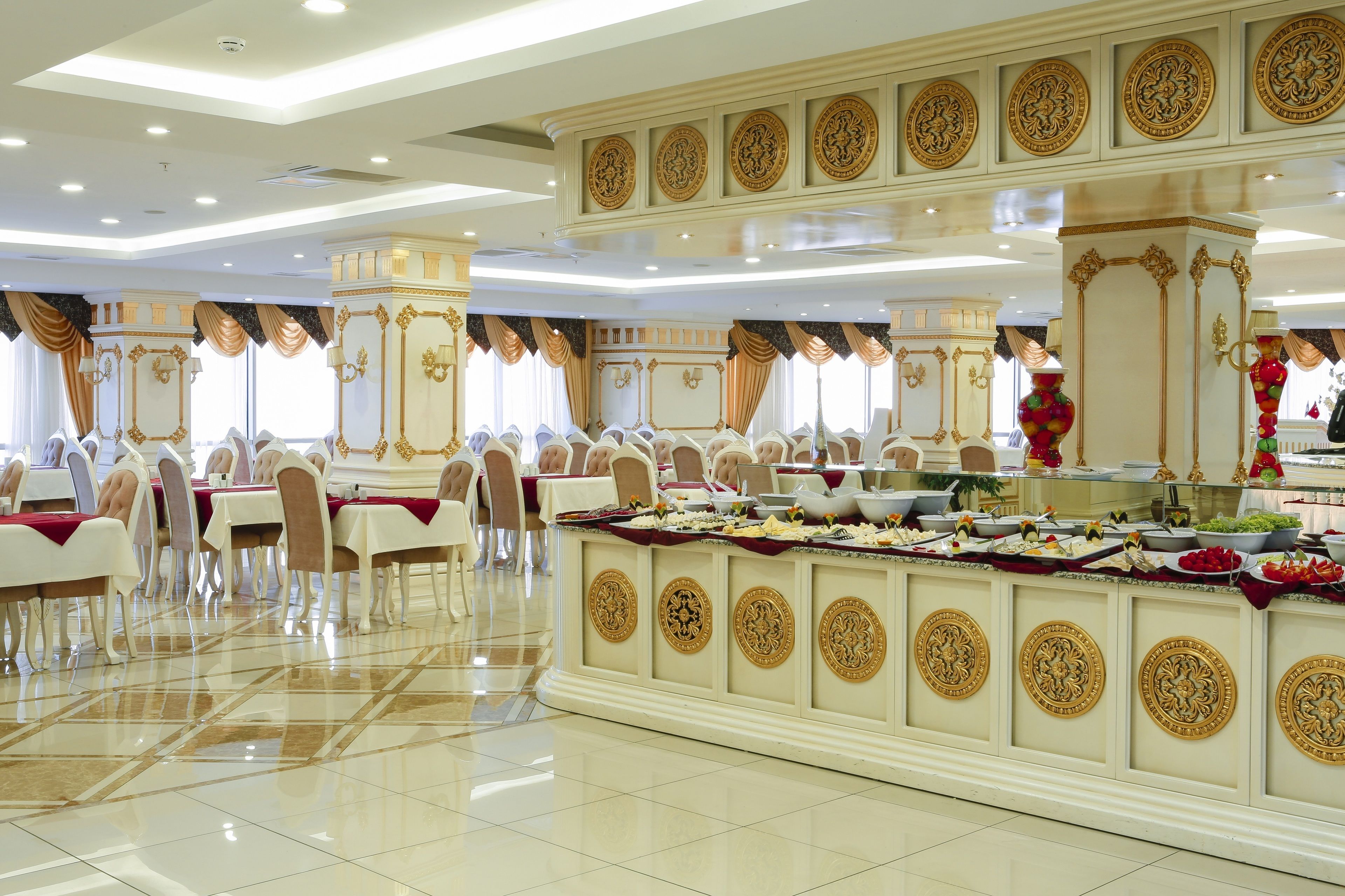 Un salón de banquetes con mesas dispuestas para una comida, una zona de bufé con alimentos y elaboradas decoraciones en las paredes.