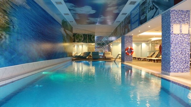 An indoor swimming pool with a mural of a wave on the wall, lounge chairs, and a lifebuoy. - World Point Hotel Istanbul (Istanbul)