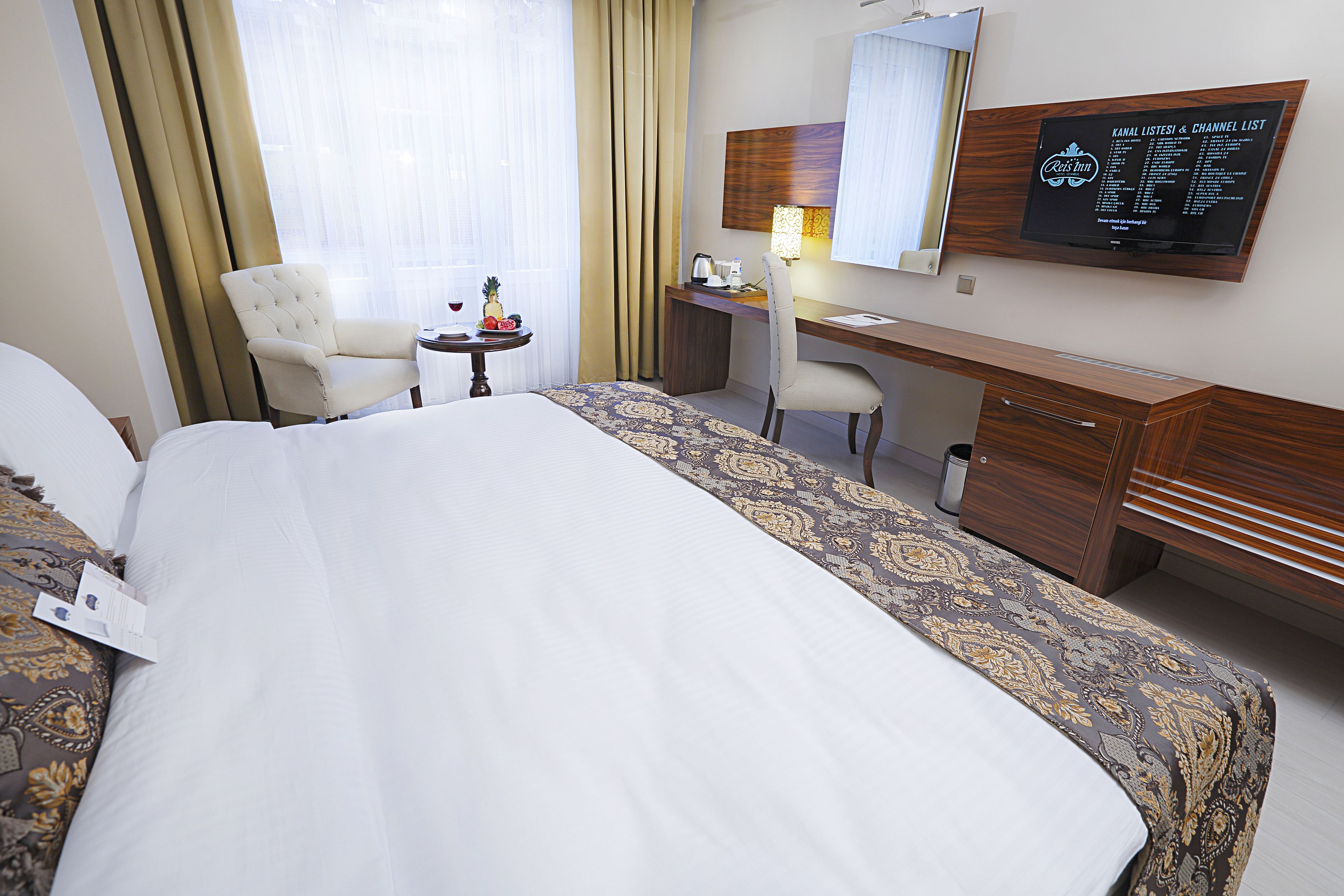 Habitación de hotel con una cama grande, un escritorio, una silla y un televisor que muestra una lista.