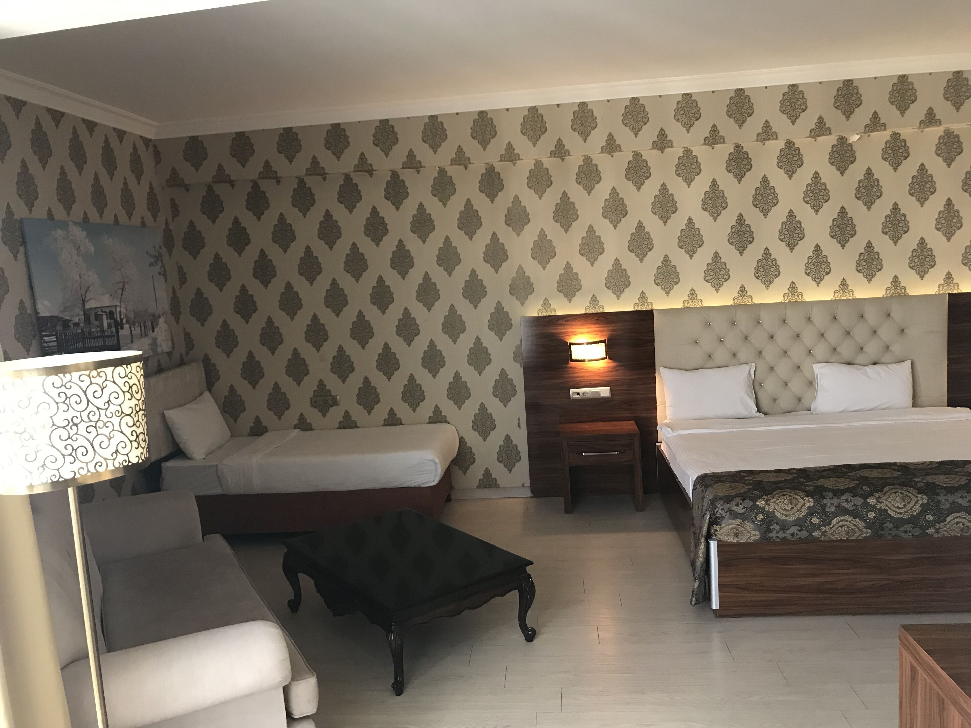 A hotel room with a bed, two bedside tables, a nightstand, a sofa, and a small table.