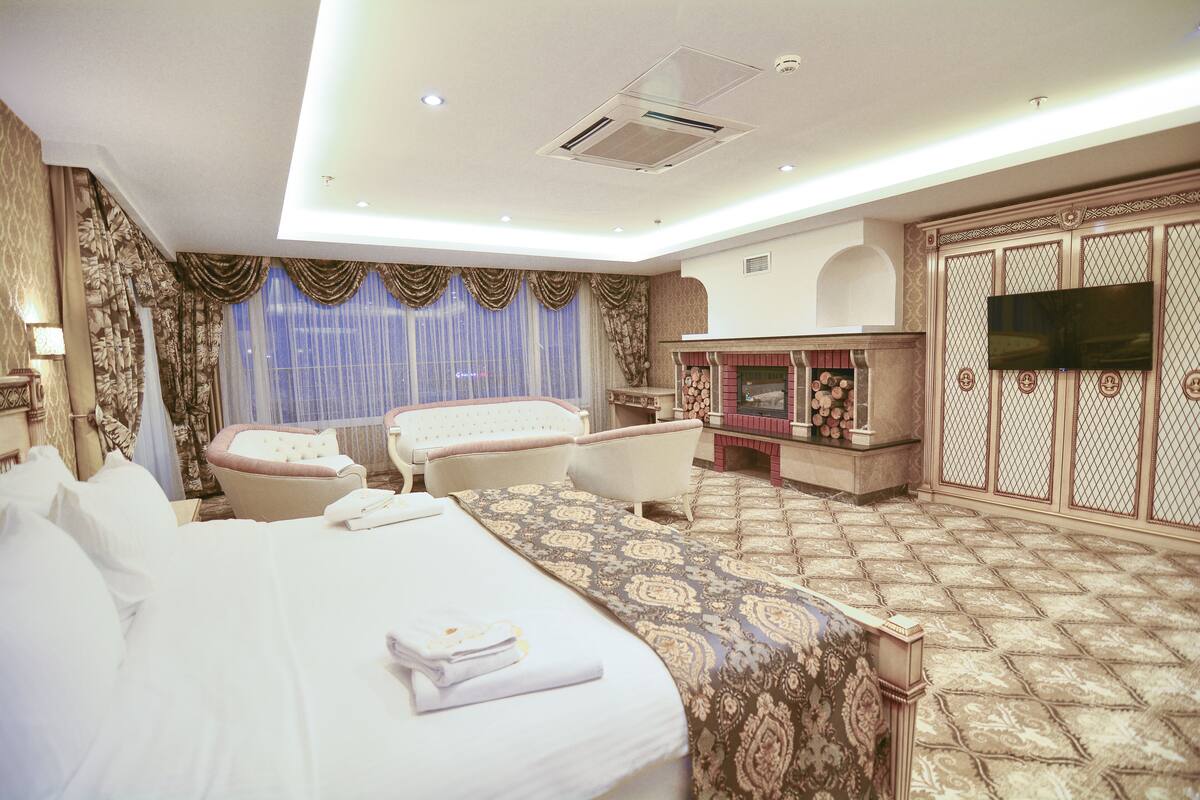 A hotel room with a large bed, two armchairs, a sofa, a TV, and a fireplace.