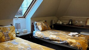Een kamer met twee bedden, dakraam, plafondventilator en nachtkastje met lamp en waterkoker.