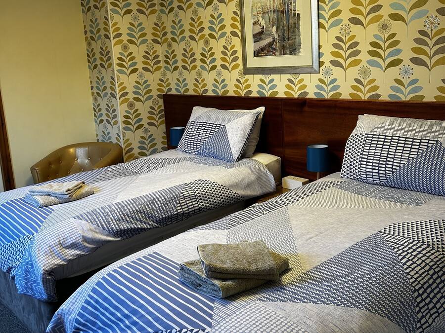 A hotel room with two beds, a headboard, a nightstand, a lamp, and a wall with a floral pattern and a framed picture.