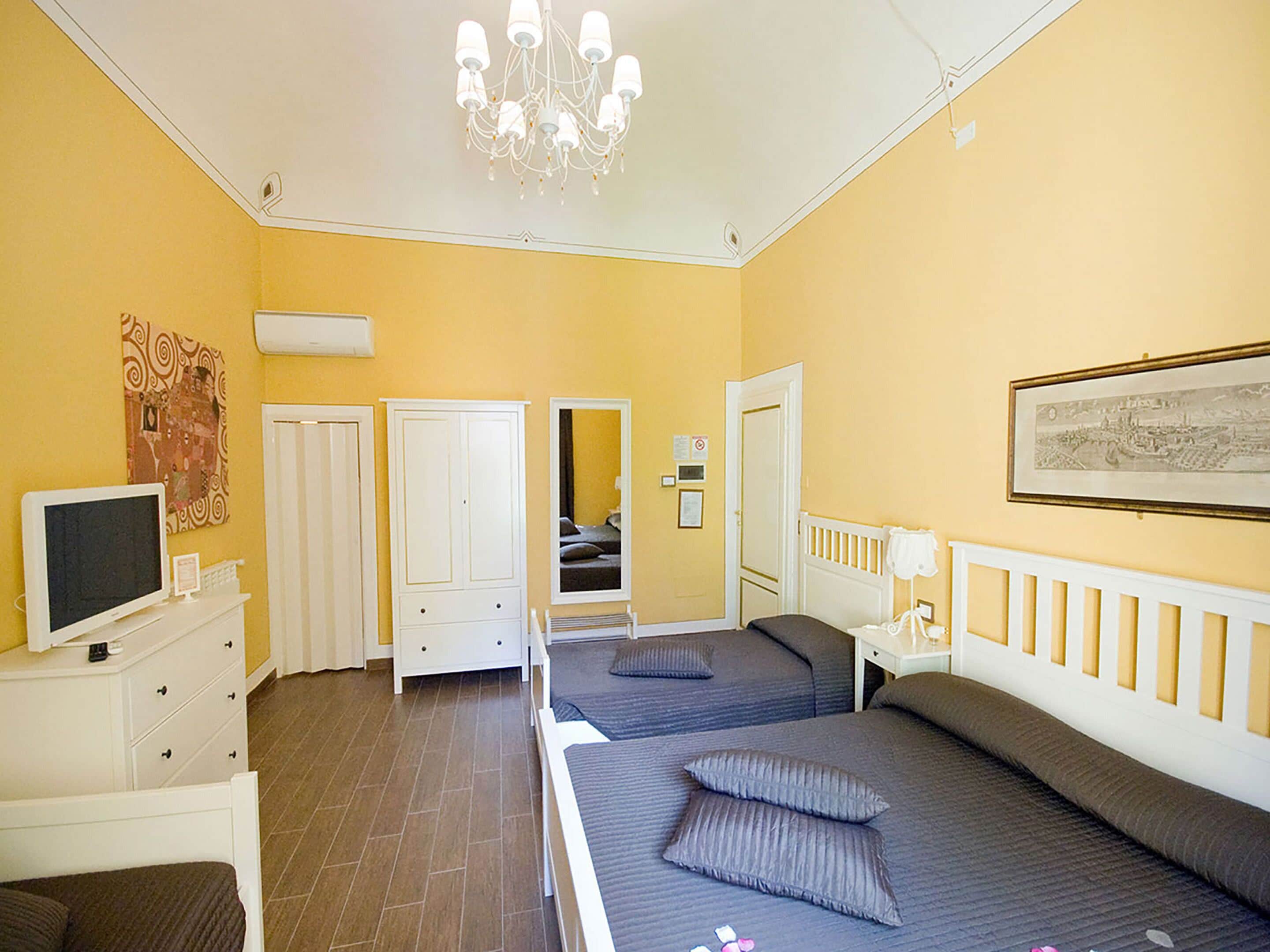 A bedroom with two beds, a dresser, a TV, and a chandelier.