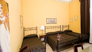 A hotel room with three beds, a desk, a chair, a lamp, and a chandelier.