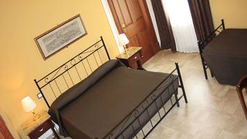 Una camera d'albergo con un letto singolo, un comodino, una lampada, un quadro appeso al muro e una porta in legno.