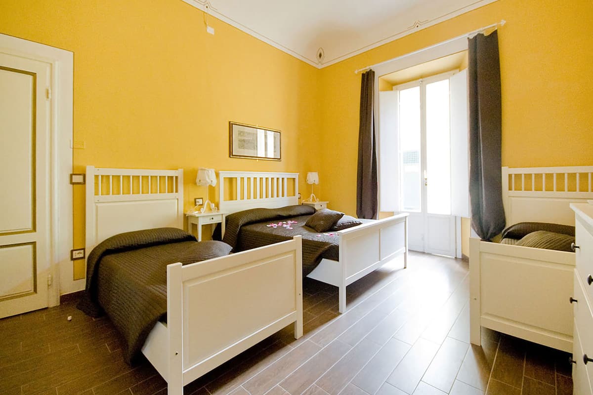 A room with two single beds, a small table, a chair, and a door.