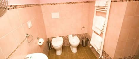 A bathroom with pink walls, a sink, two toilets, a towel rack, and a shower area.