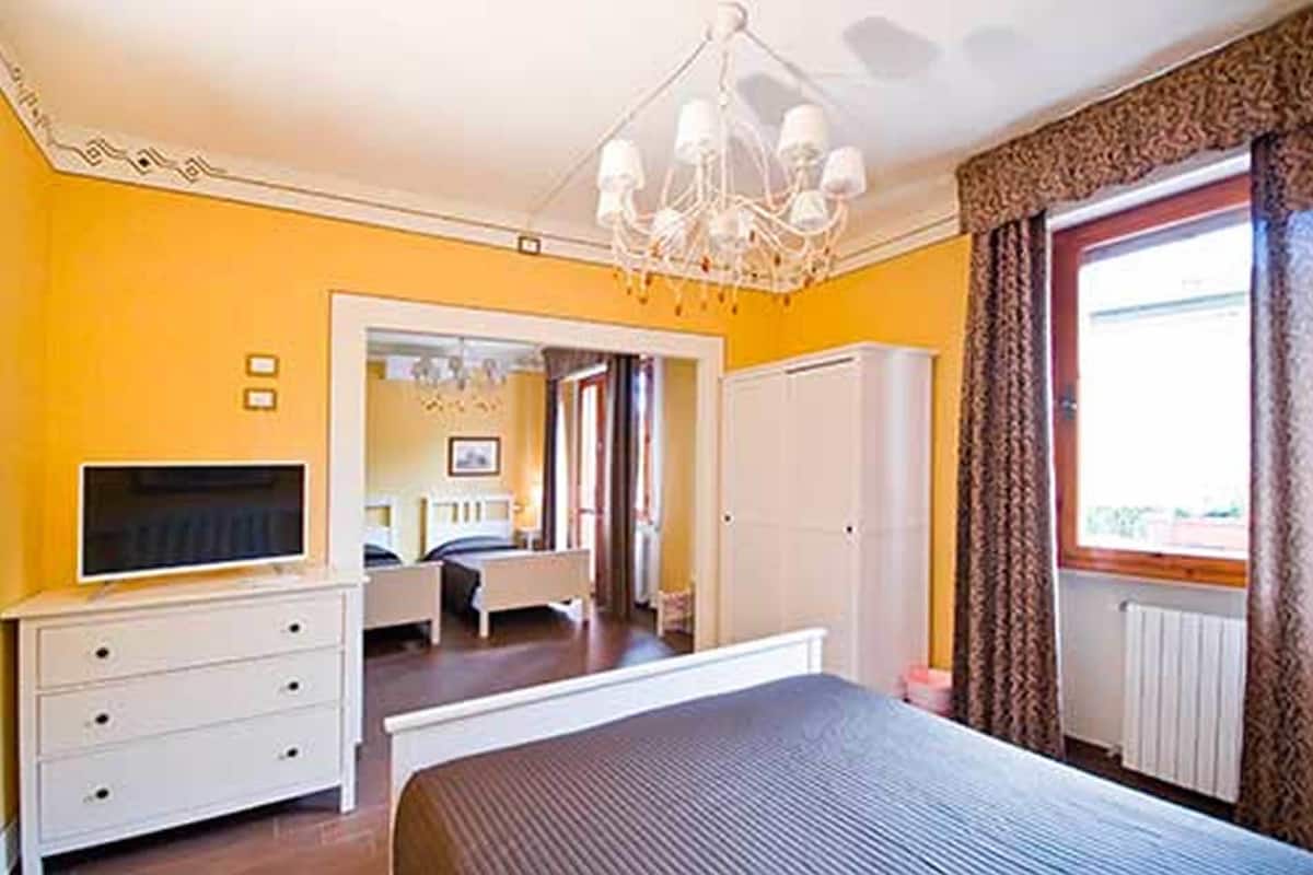A bedroom with a bed, a TV on a dresser, a chandelier, and a window with curtains.