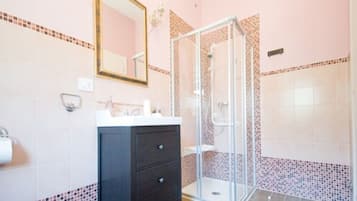 A bathroom with a glass-enclosed shower, a dark-colored vanity, and pink-tiled walls.