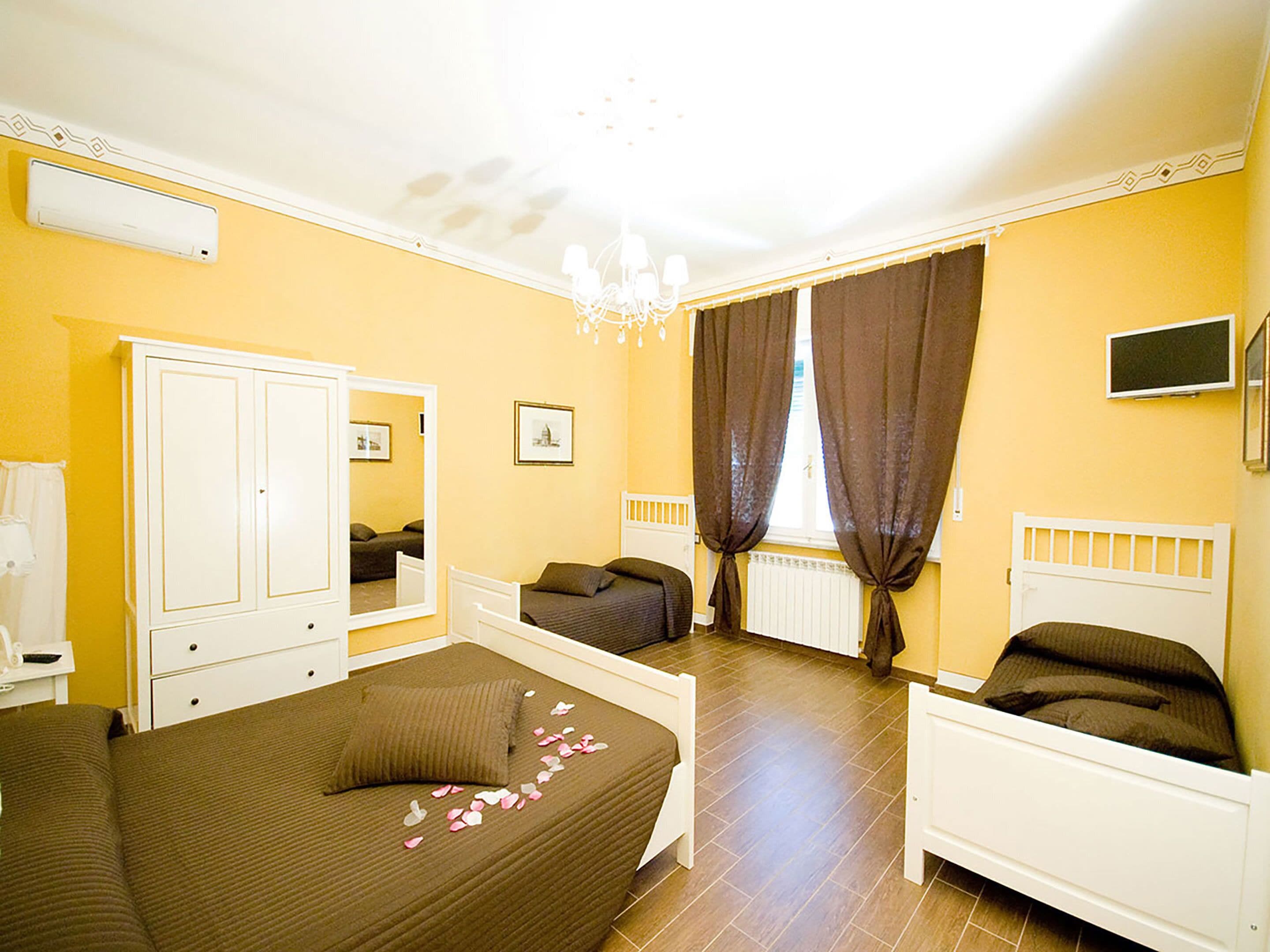 A hotel room with a large bed, a smaller bed, a wardrobe, a mirror, a television, and a window with curtains.