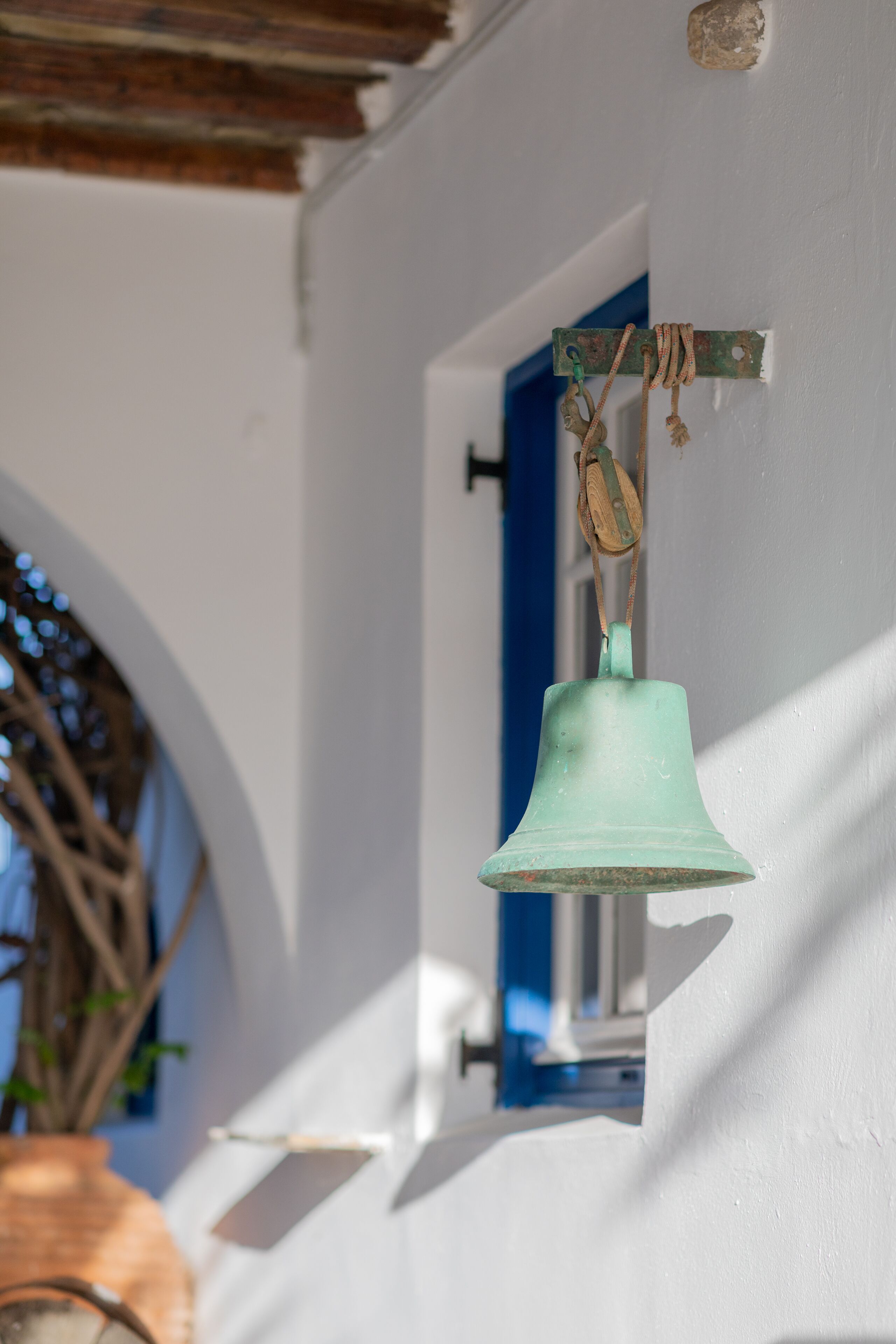 A bell hanging from a wall, a window with blue trim, and a wooden structure.