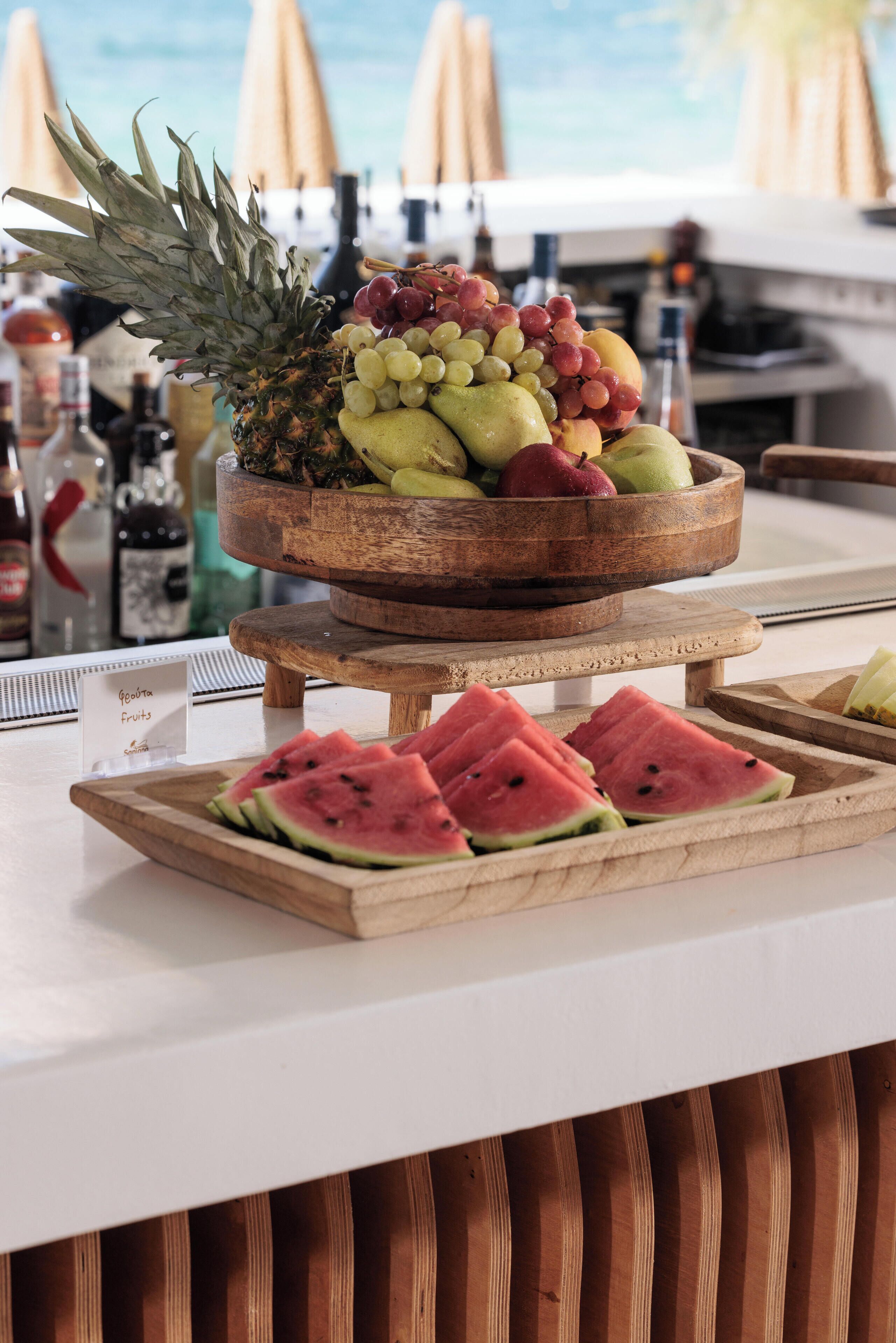 En frugtstander med ananas, druer og vandmelon på et træbord.