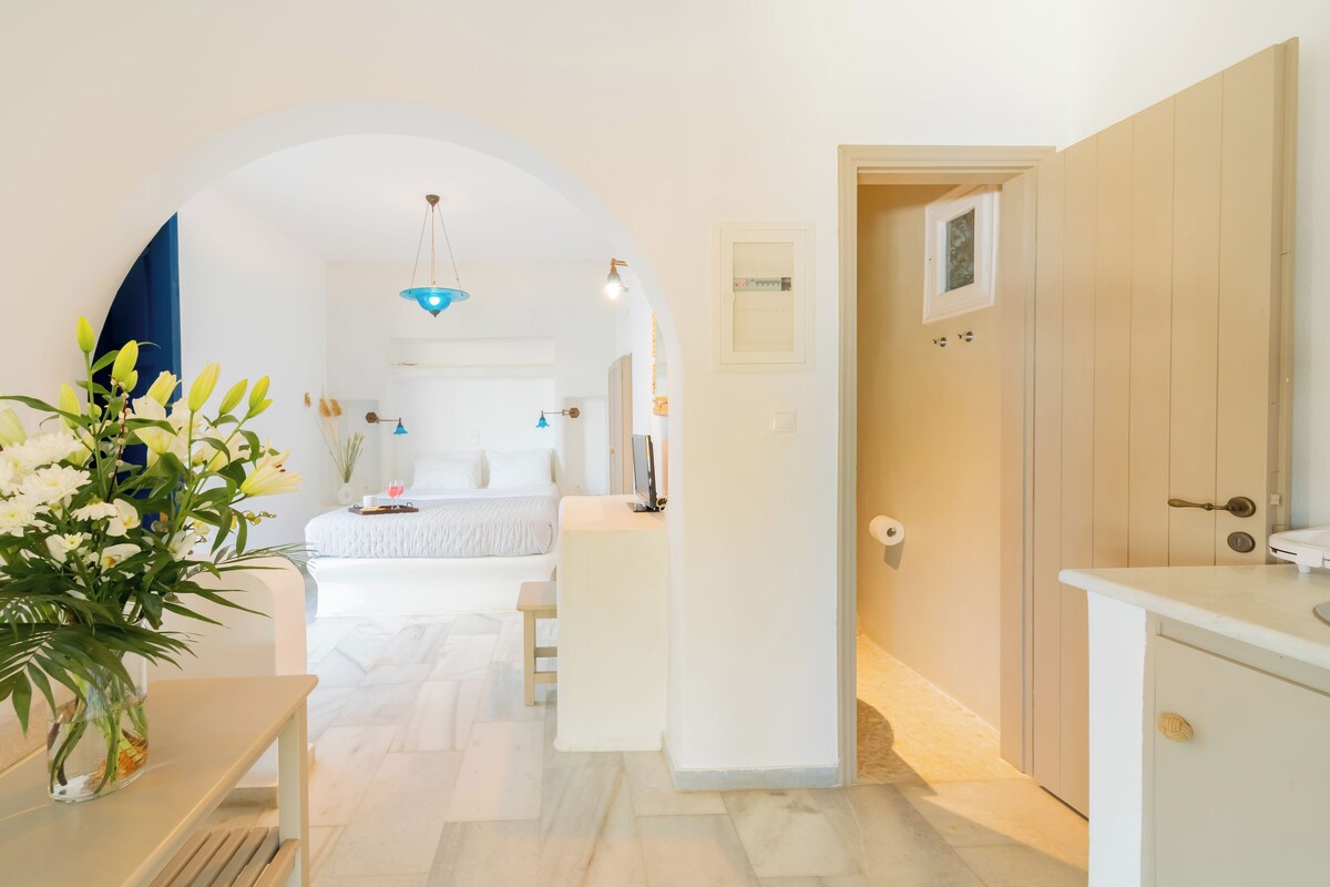 Een moderne hotelkamer met een bed, een klein bureau, een bloevas en uitzicht op de gang.