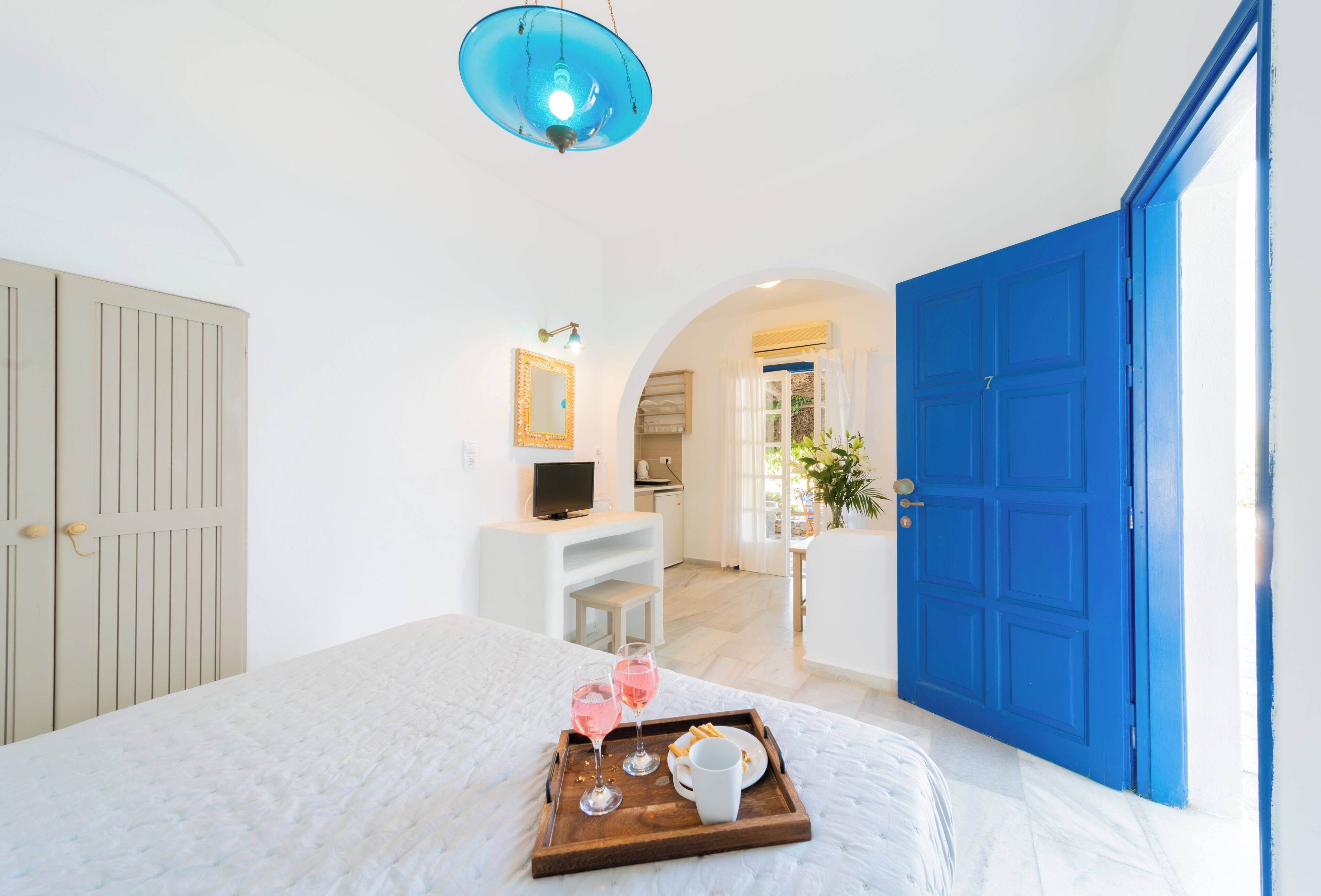 Quarto com cama, bandeja com petiscos e bebidas, televisão e porta azul.