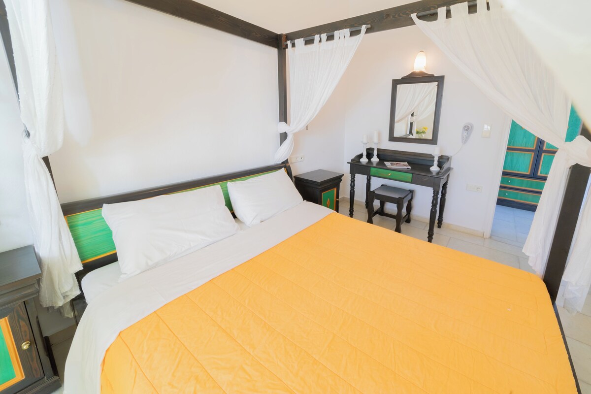Een slaapkamer met een bed, bureau, stoel en spiegel.