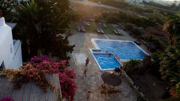 A rooftop pool area with multiple swimming pools, lounge chairs, and a stone patio.