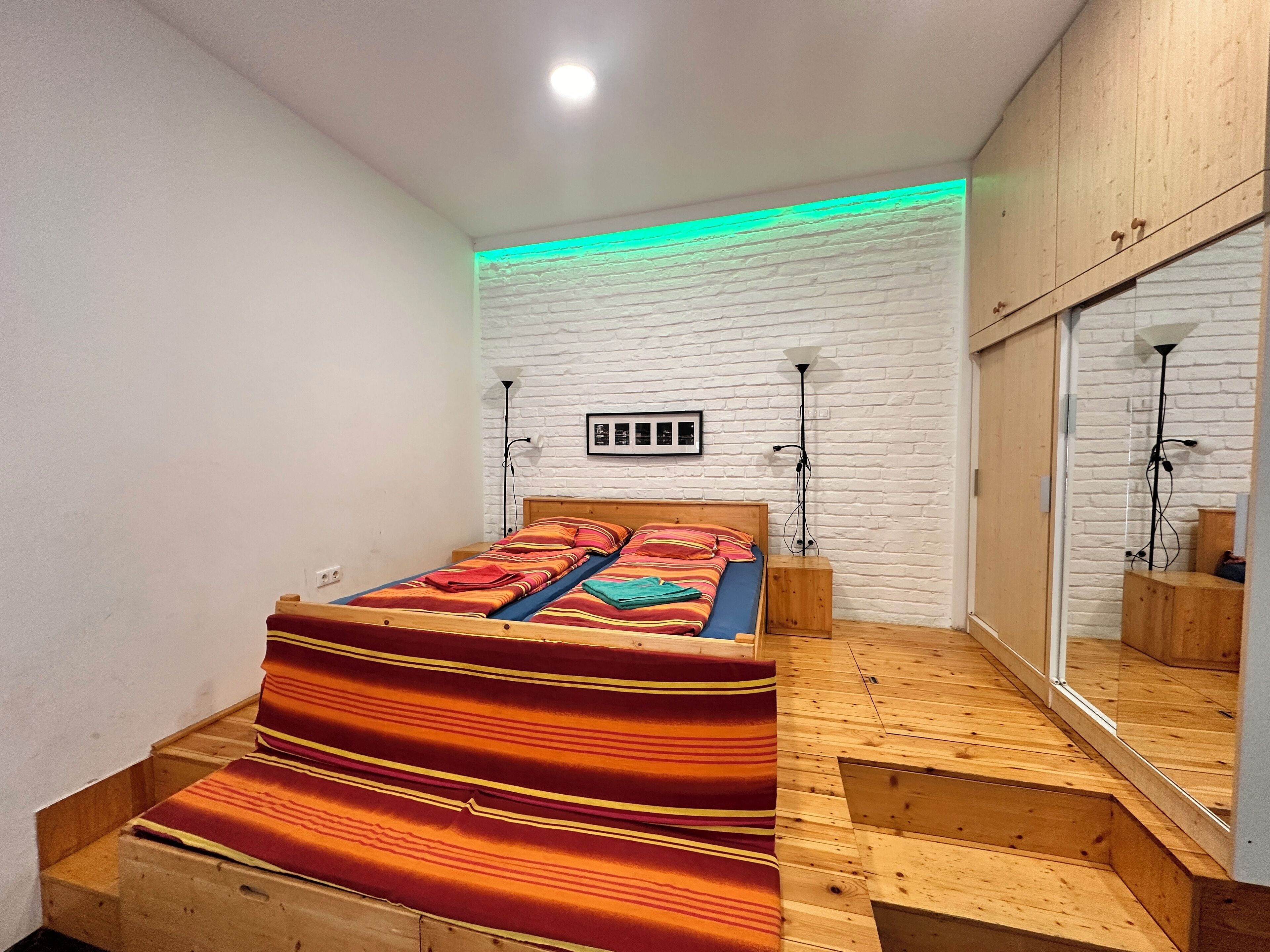 Een slaapkamer met een houten bed, een witte baksteenmuur en een spiegelkast.