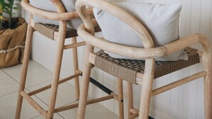 Uma cozinha com banquetas de madeira, micro-ondas e prateleira com planta e objetos decorativos.