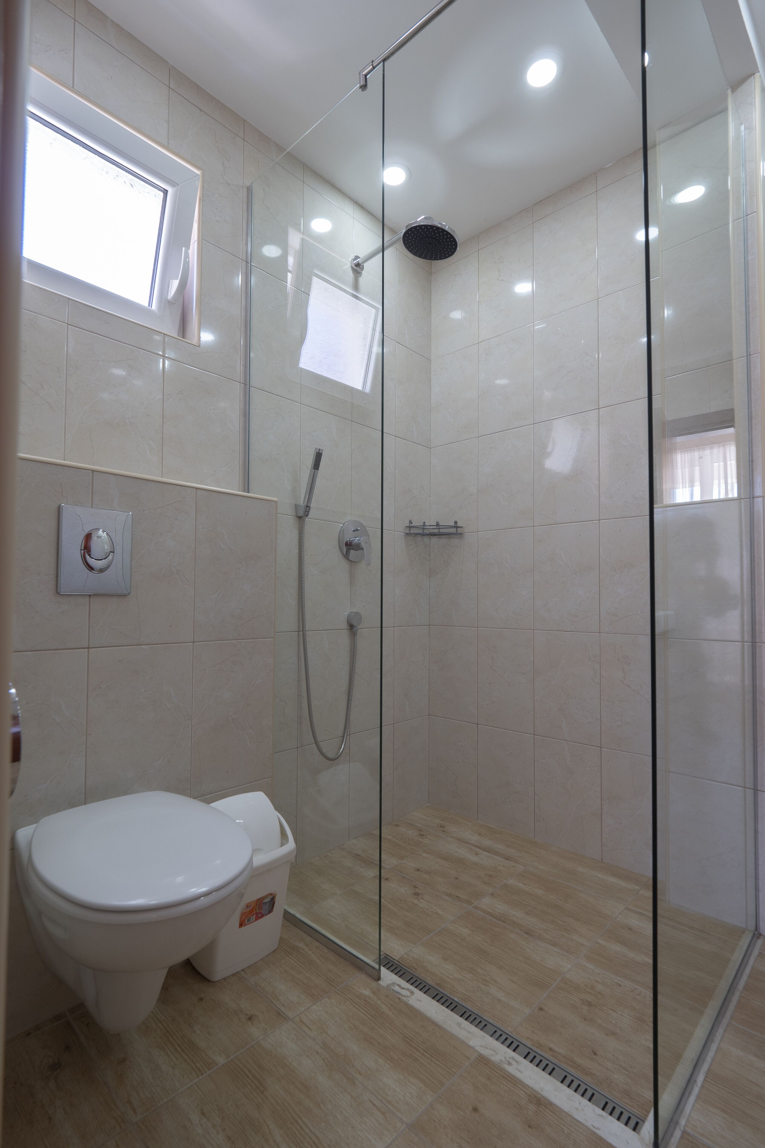 A modern bathroom with a glass-enclosed shower, a toilet, and a wall-mounted faucet.
