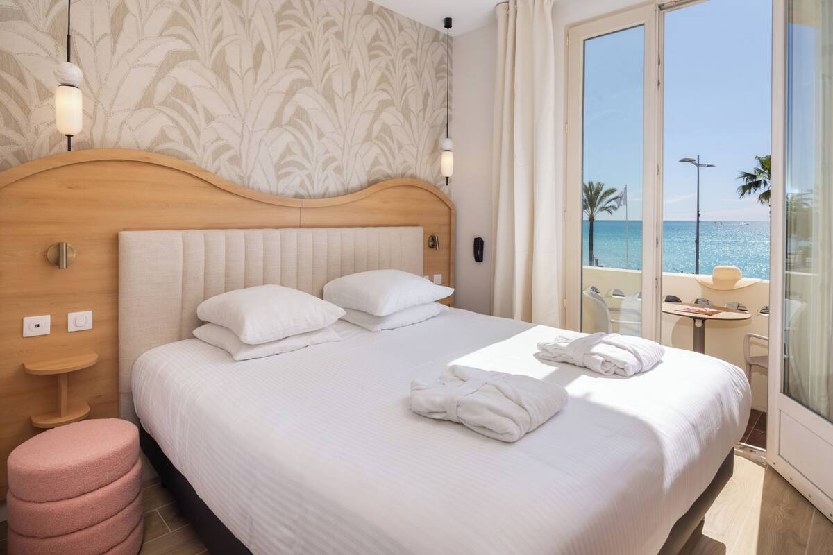 Une chambre d’hôtel avec un grand lit, une tête de lit en bois, une petite table ronde et une vue sur la mer.