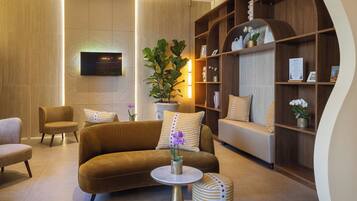 Una sala de estar moderna con un sofá, sillones, una mesa de centro, un televisor montado en la pared y una estantería de madera.