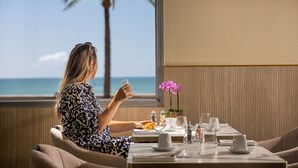 A person dining at a table with a view of the ocean and palm trees. - Hotel Royalmar (Cagnes-sur-Mer)