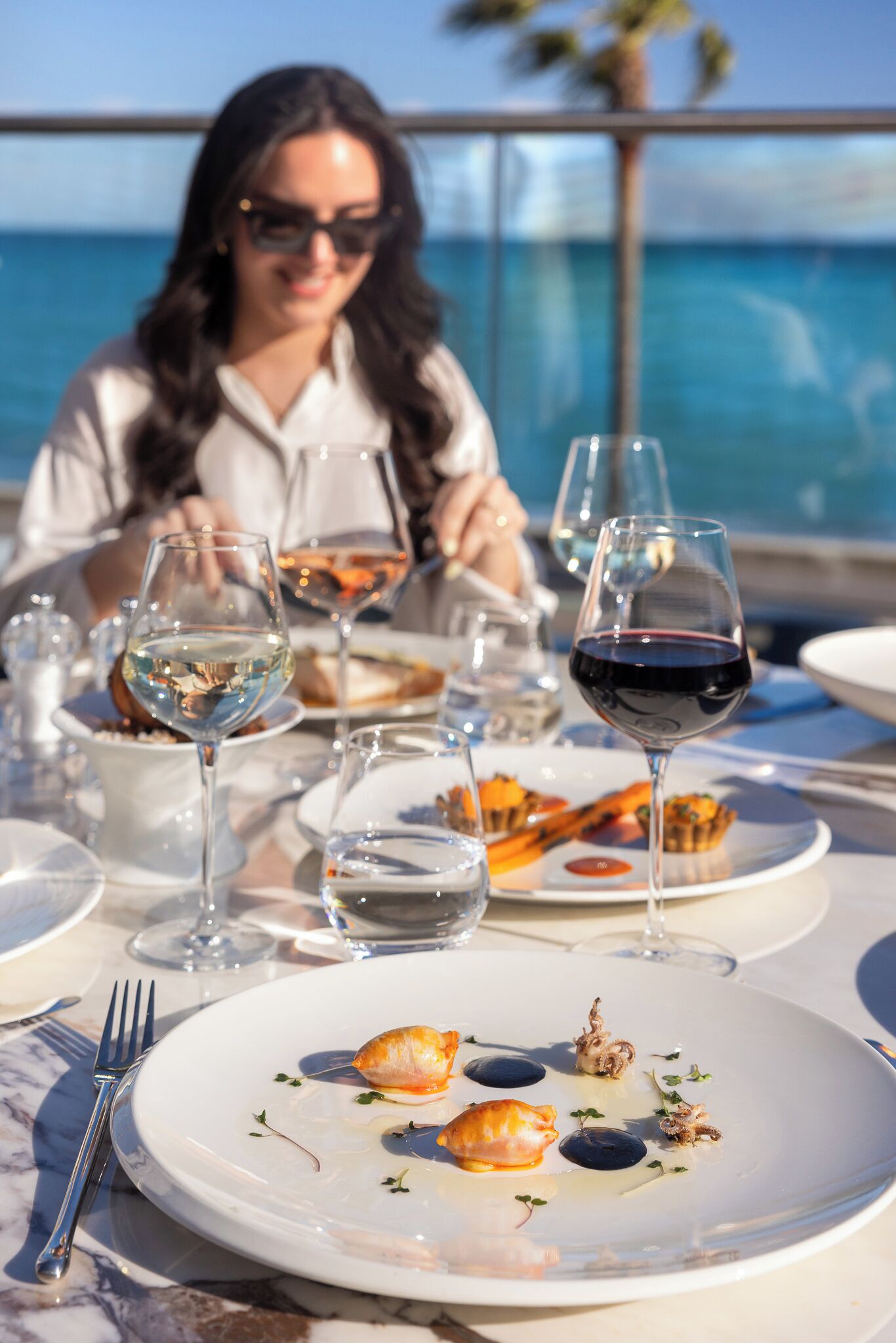 A dining table with plates of food, wine glasses, and a fork.