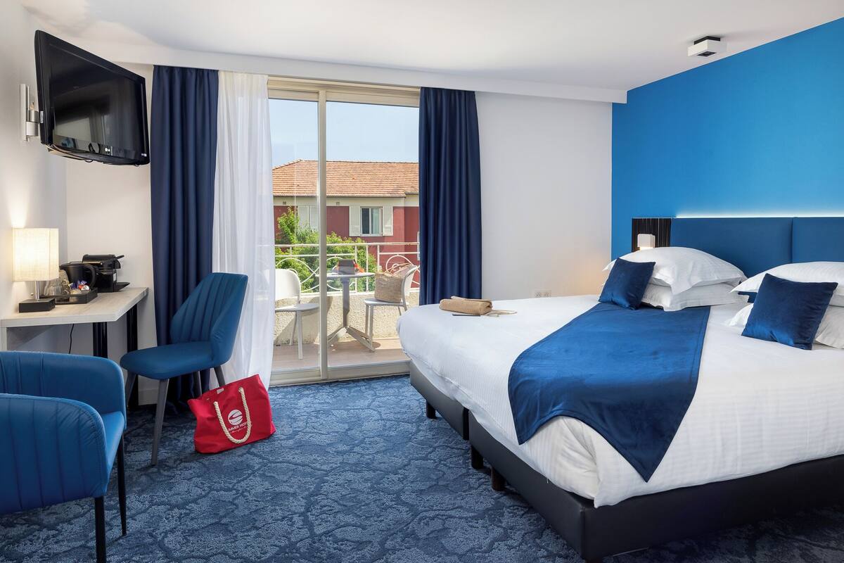 Une chambre d’hôtel avec un lit, un bureau, une chaise, une télévision et un balcon avec vue.