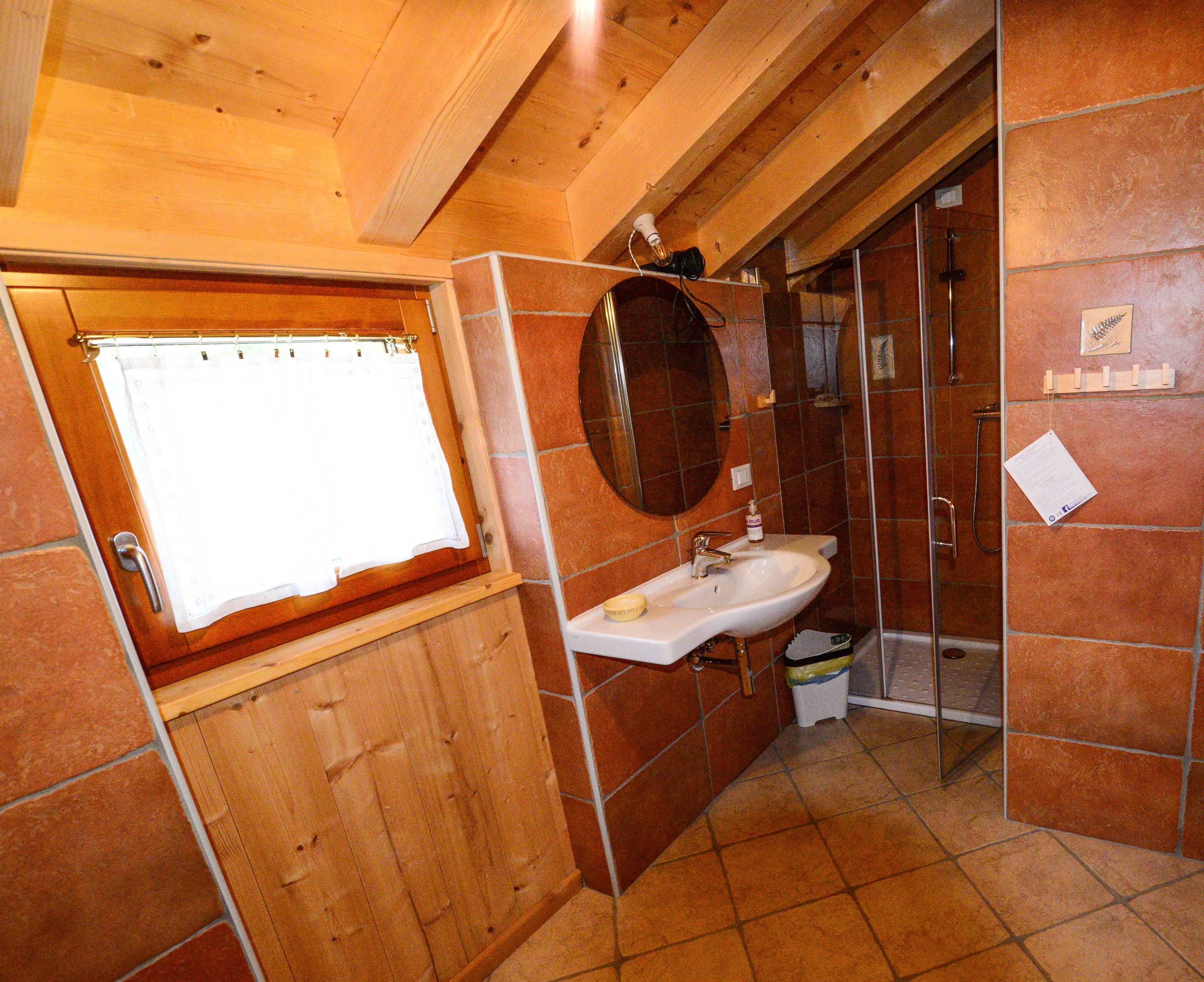 A bathroom with wooden walls, a white sink, a mirror, and a shower area.