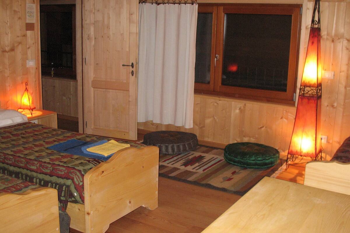 Ein gemütliches Zimmer mit Holzwänden und Holzdielen, ausgestattet mit zwei Betten aus Holz, einem Fenster mit Vorhängen und zwei Wandleuchten.